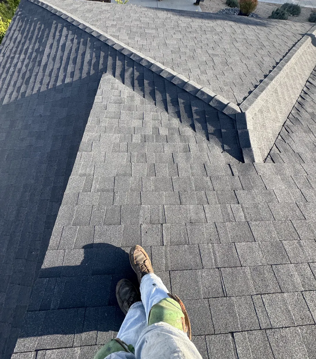 Standing on a finished architectural shingle roof, looking down the hip toward the eave.