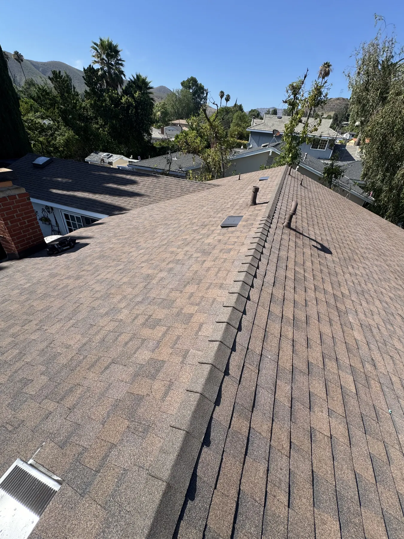 Finished architectural shingle reroof on a hillside home, looking along the ridge toward the mountains.