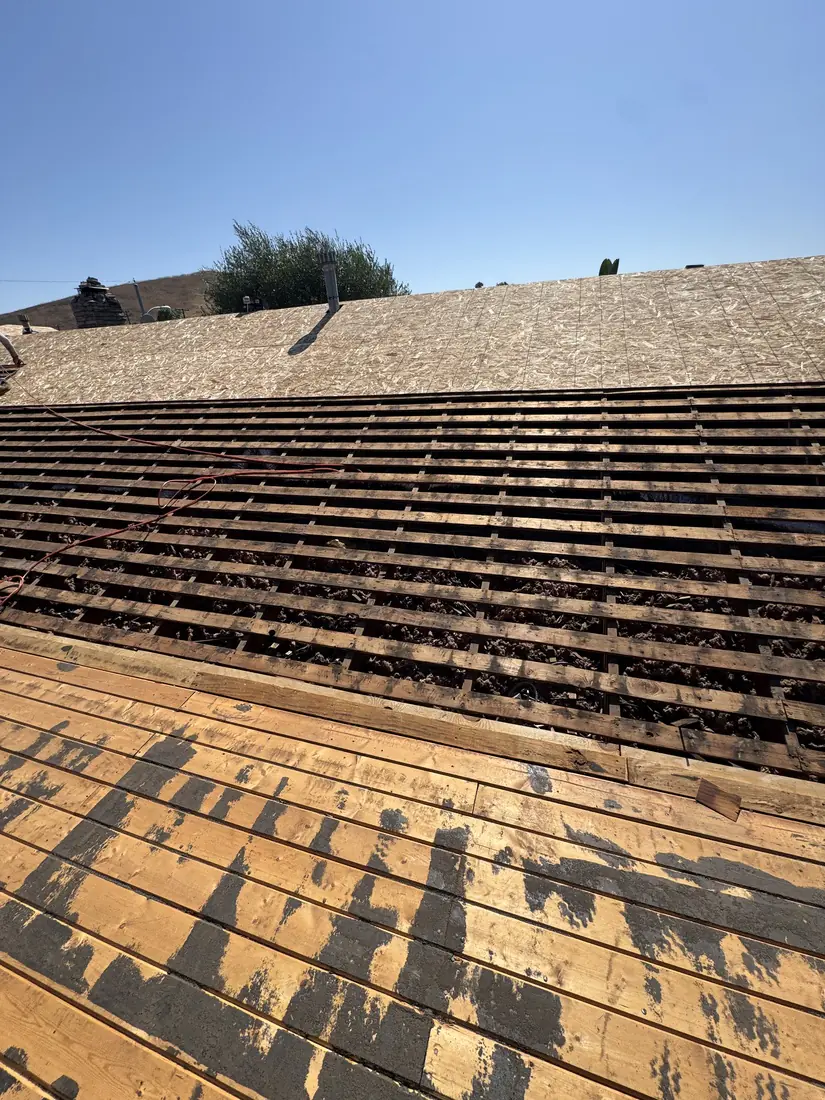 Open skip sheathing exposed across a slope with new plywood already laid on the section above.