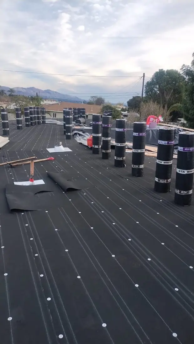 Base sheet fastened across a flat roof with rolls of cap sheet standing ready to go down.